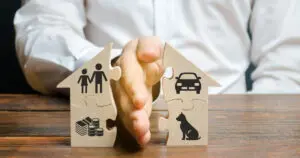 Male hand separating puzzle house with images of property, children & pets, representing property division. MBH Fort Worth | Family Law